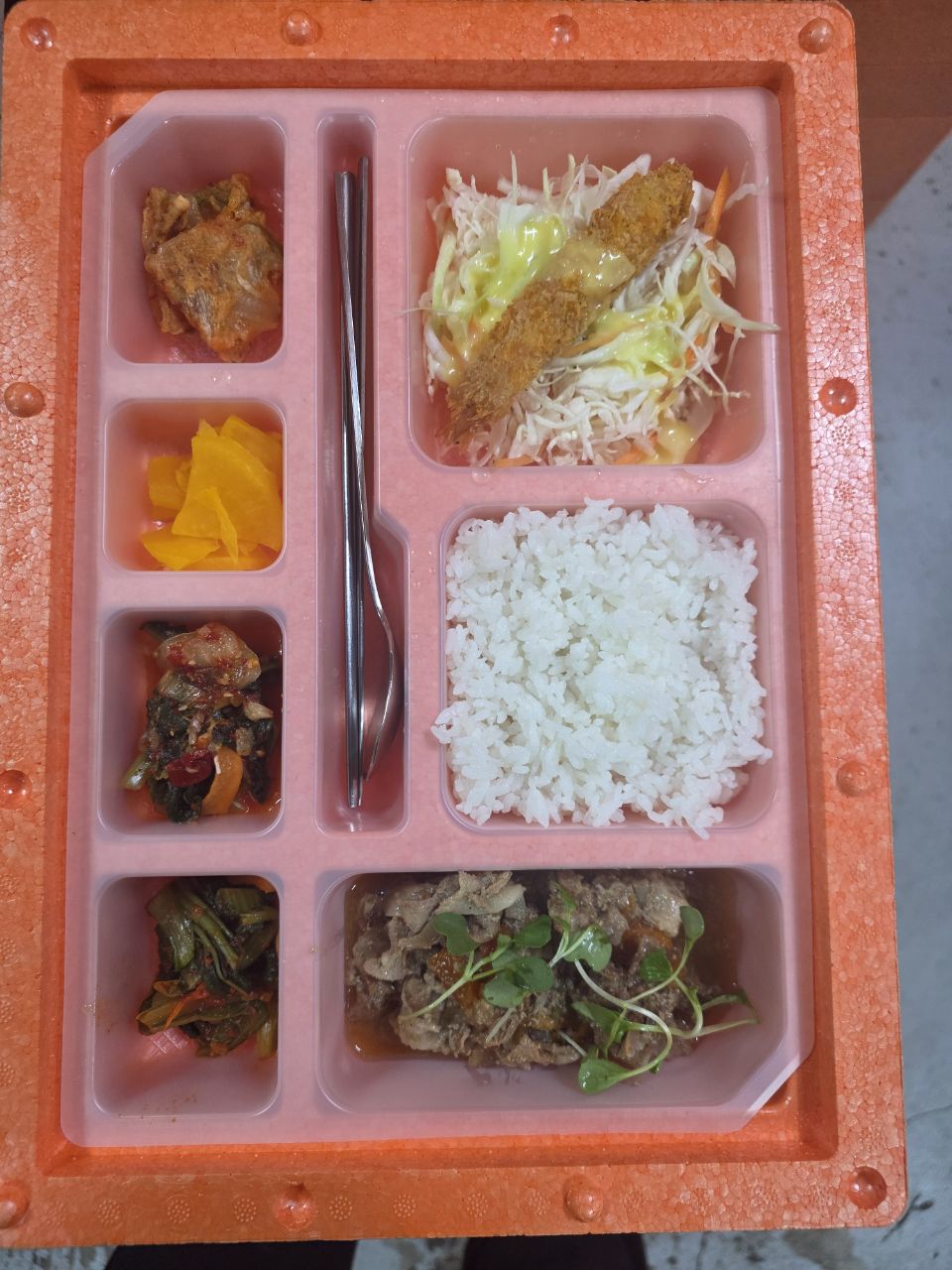 주황색 보온 용기에 담긴 우와푸드 도시락. 흰쌀밥, 불고기, 새우튀김 양배추 샐러드, 김치와 단무지 등 반찬 4가지, 수저